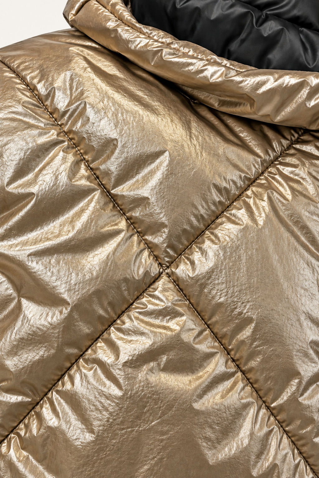 Close-up of a metallic gold puffer jacket with diamond-quilted stitching and a black inner lining visible at the collar.