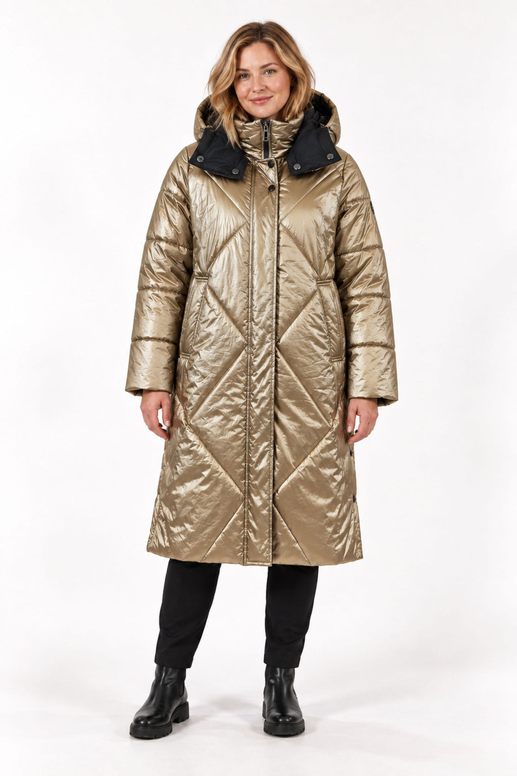 A woman modeling a long, shiny quilted coat in metallic gold with a contrasting black hood, standing against a plain white studio background.