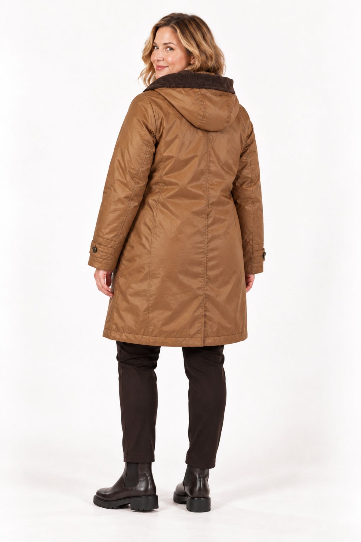 A woman shown from the back wearing a mid-length brown hooded coat with a dark brown faux-fur collar, paired with dark pants and black boots, against a plain white studio background.