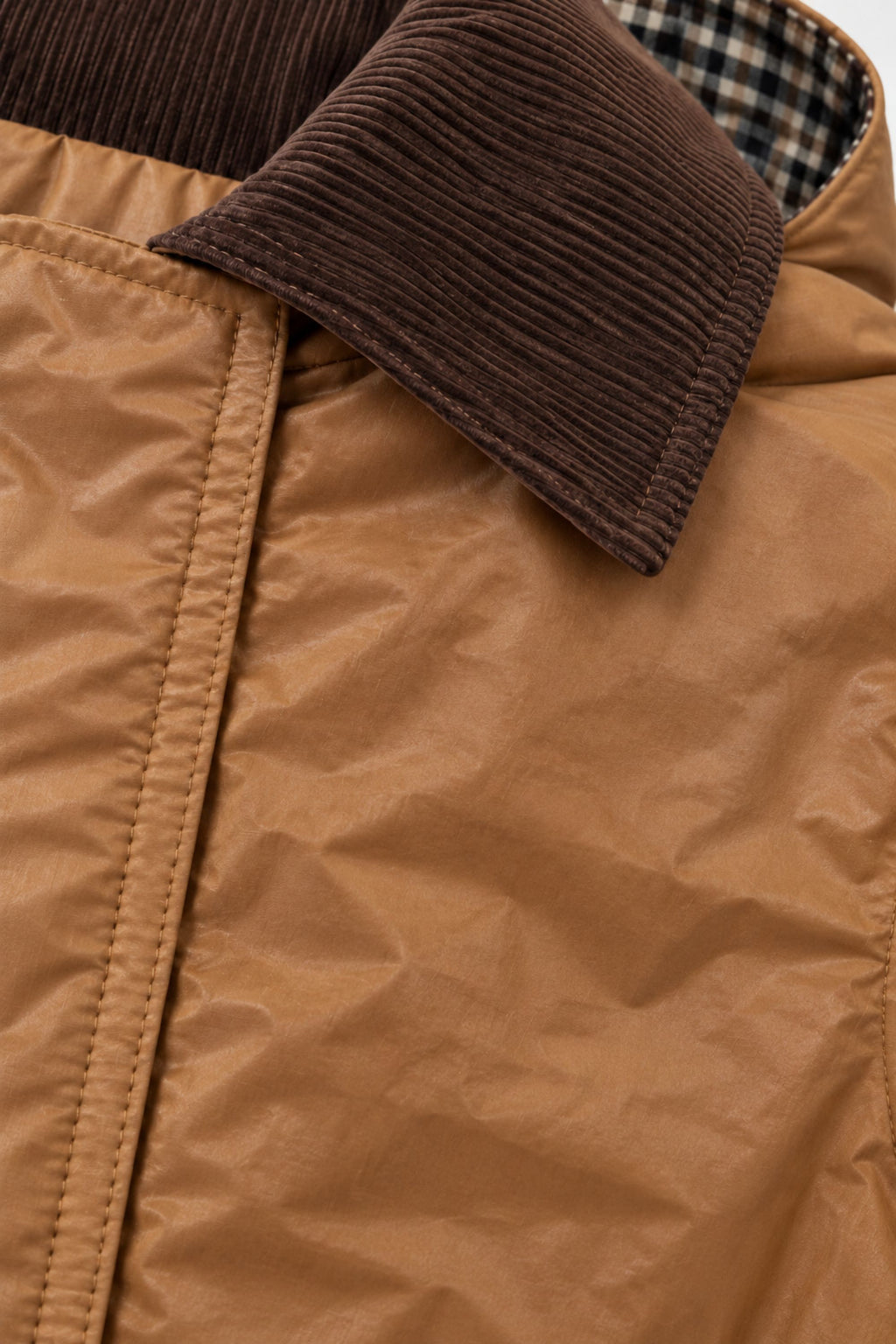Close-up of a tan waxed fabric jacket with a dark brown corduroy collar and a plaid lining visible inside the collar.