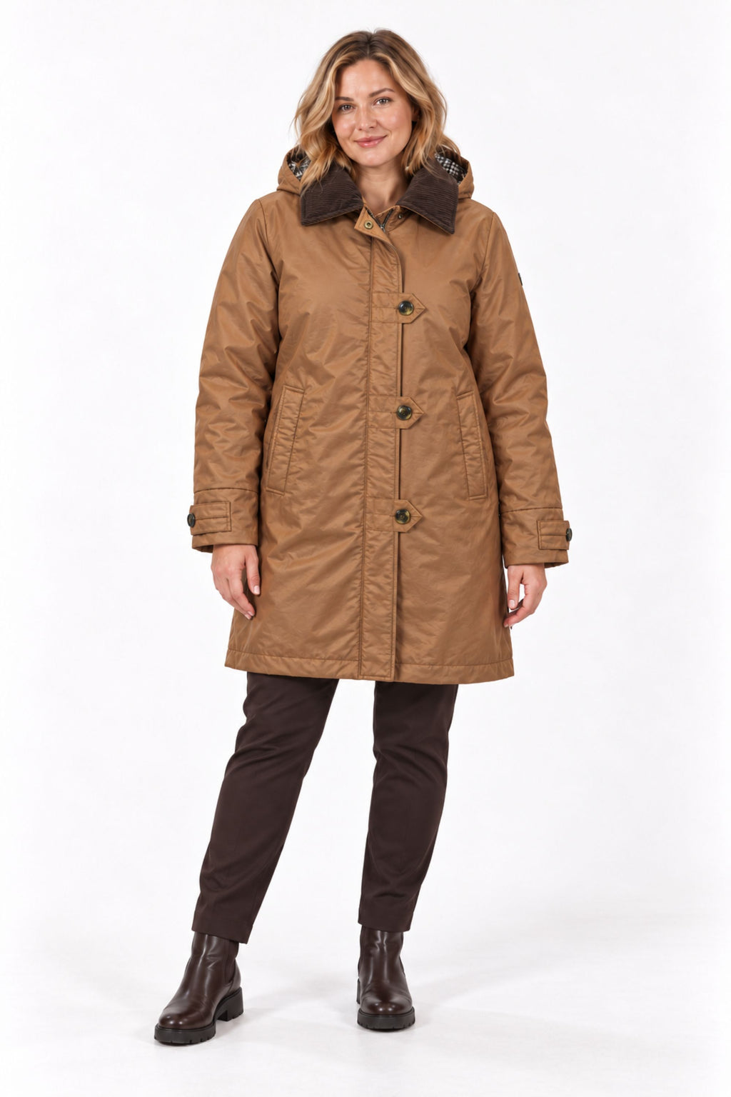 A woman modeling a mid-length brown waxed canvas parka with a dark brown faux-fur collar, paired with dark brown trousers and boots, against a plain white studio background.