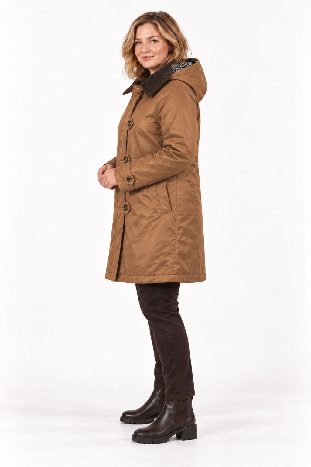 A woman modeling a mid-length brown hooded coat with dark buttons and a dark collar, paired with dark pants and brown ankle boots, against a plain white studio background.