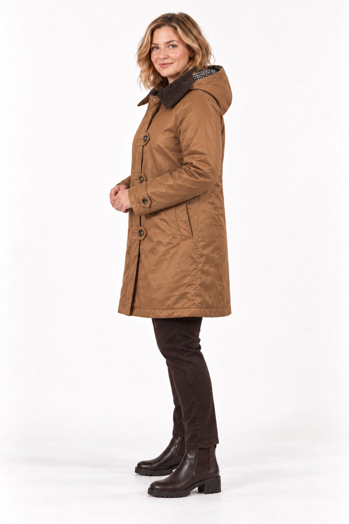 A woman modeling a mid-length brown hooded coat with dark buttons and a dark collar, paired with dark pants and brown ankle boots, against a plain white studio background.